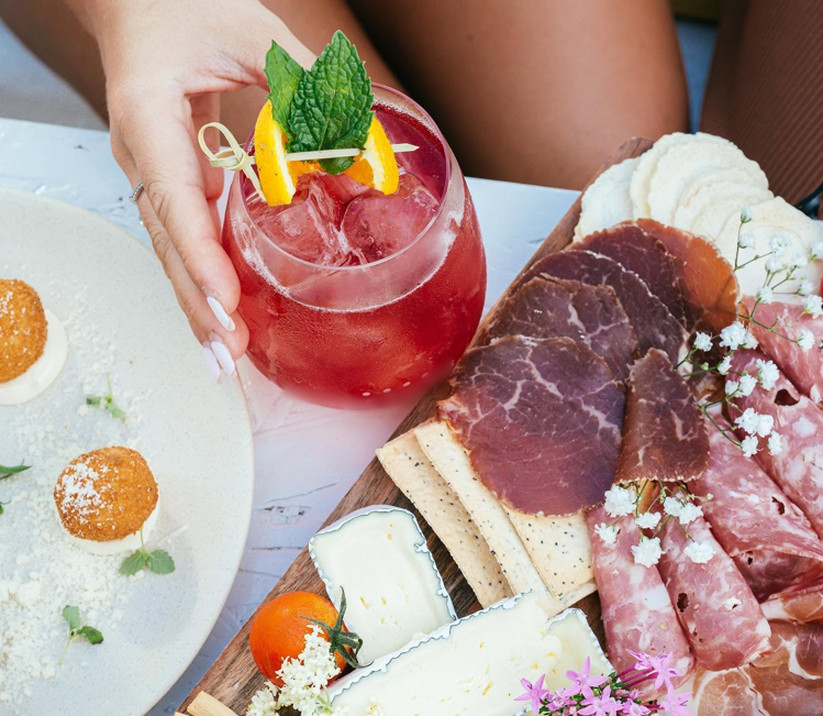 Cocktails beside a charcuterie board of cheeses, cured meats and fruit