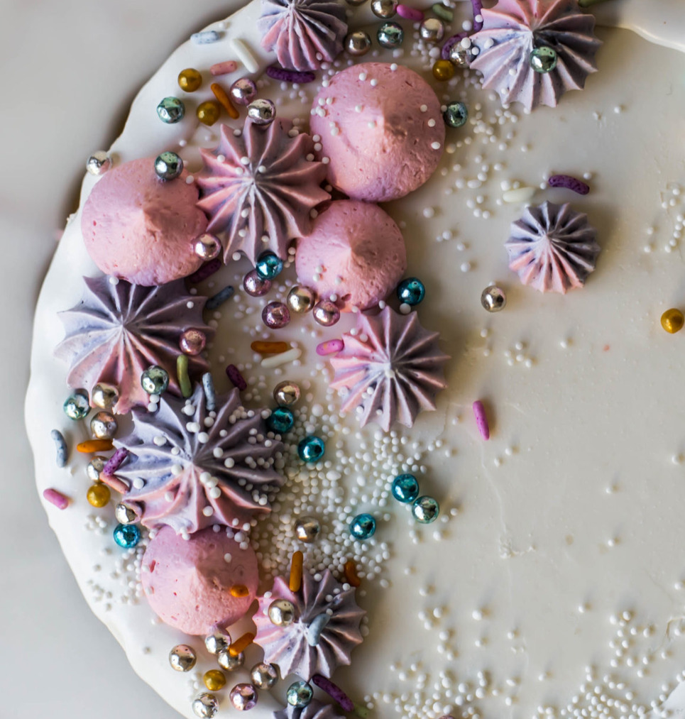 Close-up of a white cake top with meringue kisses and metallic sprinkles