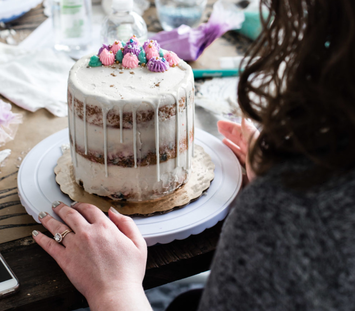 A hand turning a white drip cake topped with pastel buttercream rosettes