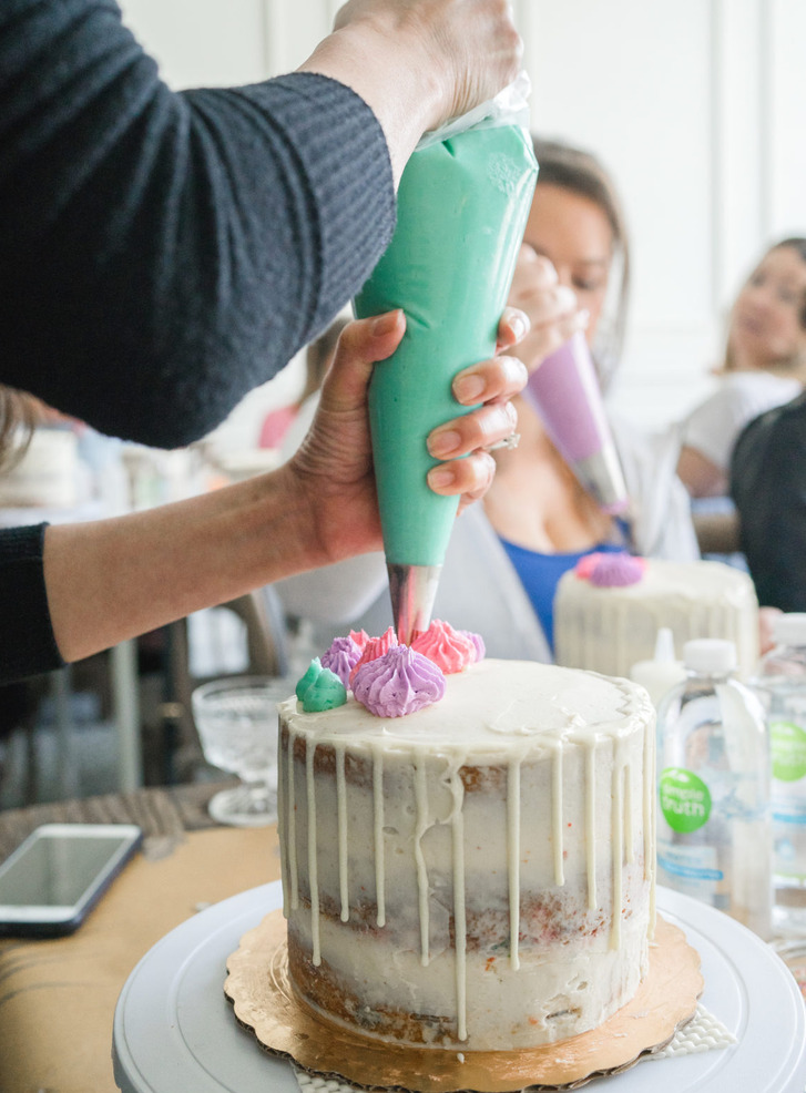 Hands piping pastel buttercream rosettes onto a white drip cake