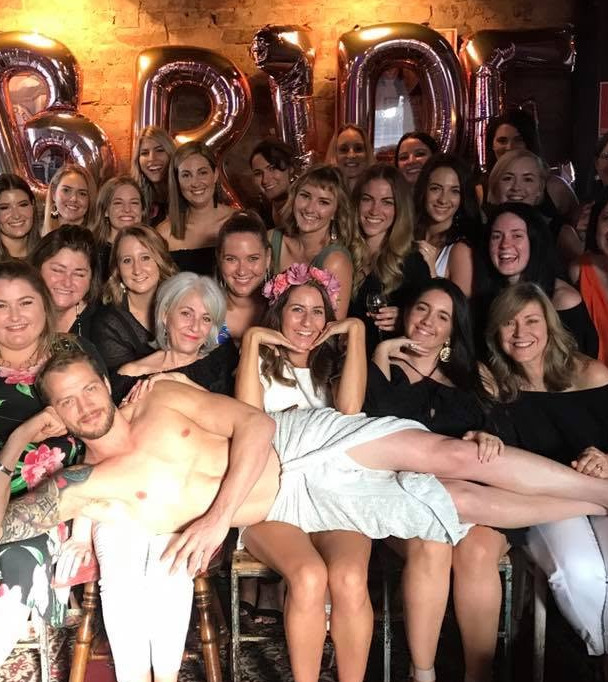 A big hens group under BRIDE balloons with the model lying across their laps