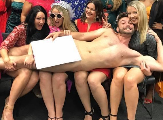 The bride in a tiara and sunglasses with the model lying across the group, a drawing board over him