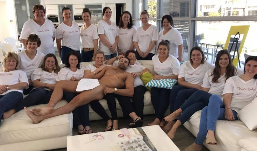 Hens in matching white bride tribe tees with the model across their laps on a white couch