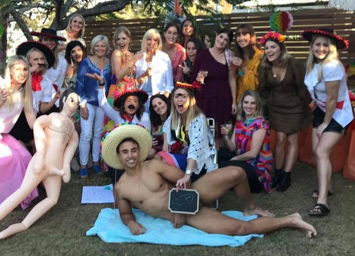 A fiesta themed hens group in sombreros with the model lying on a towel holding a chalkboard