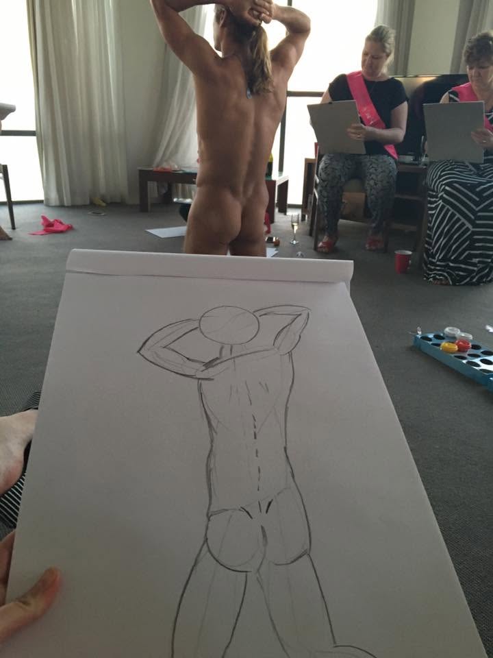 A sketch pad in the foreground with a drawing of the model, who poses with his back to the room