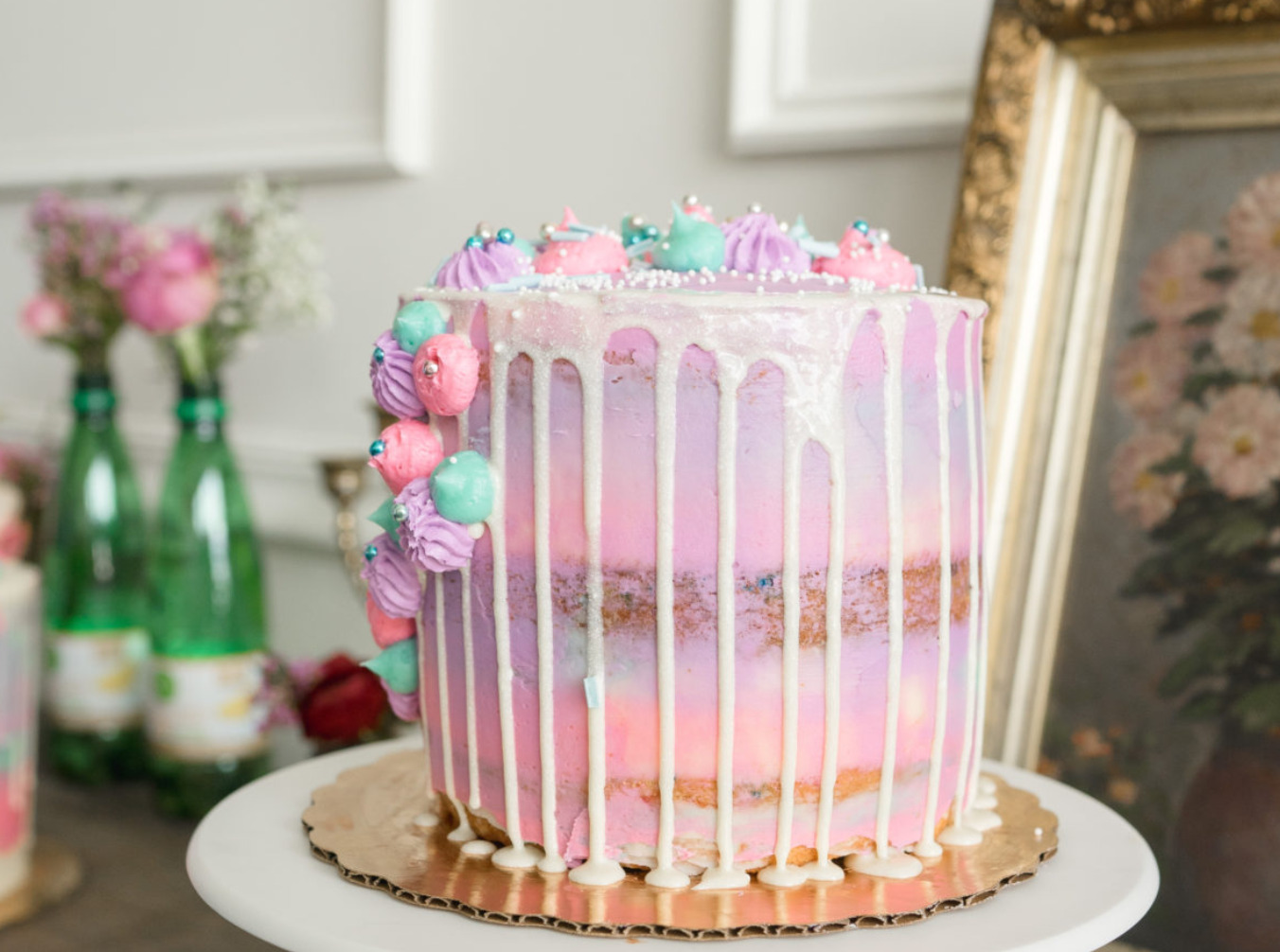 A pink and purple drip cake topped with meringue kisses and sprinkles