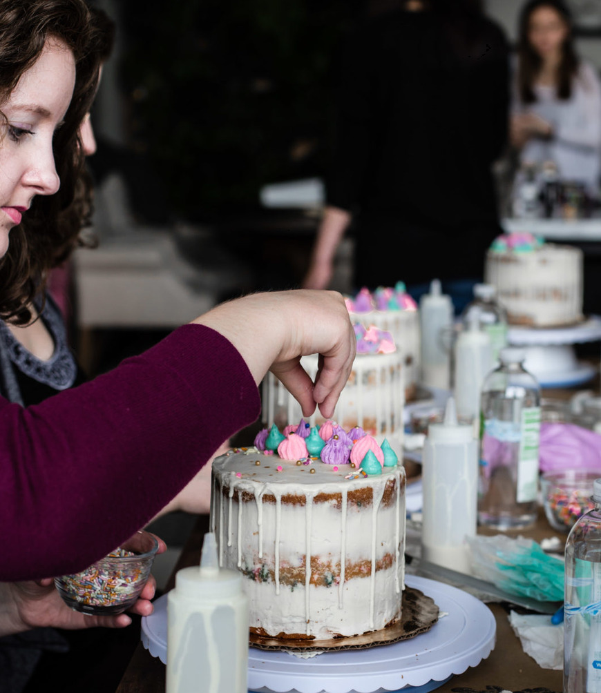 A woman placing meringue kisses on a drip cake with a bowl of sprinkles