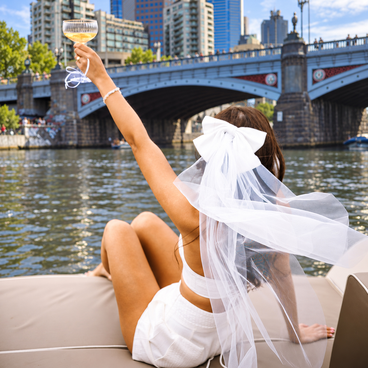 A bride to be in a bow veil raising a glass on a boat on the river in Melbourne