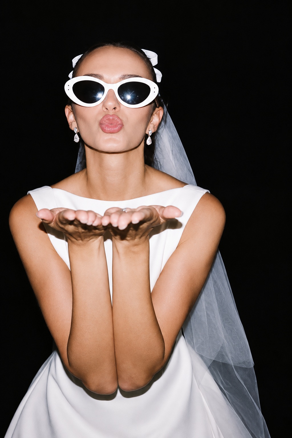 The bride in a veil and white sunglasses blowing a kiss