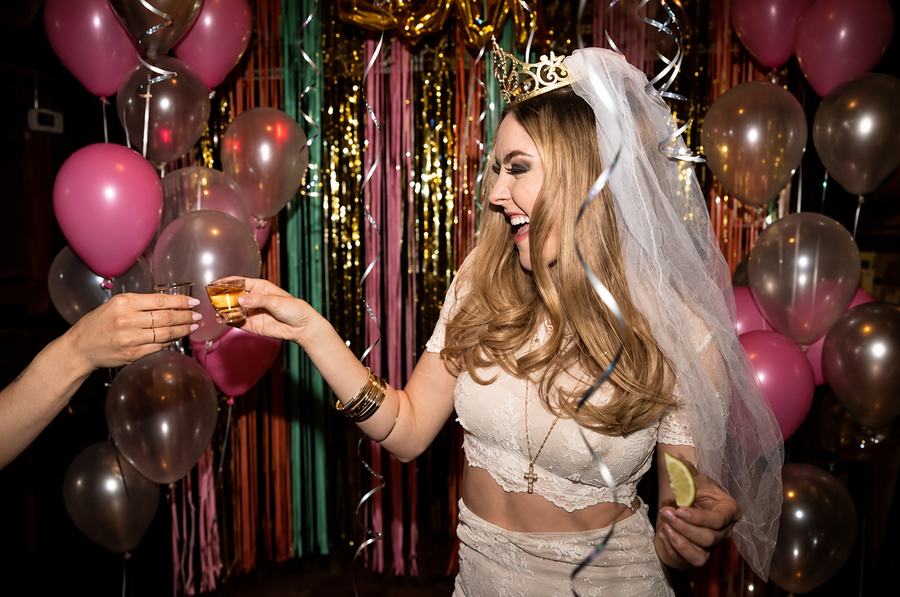 A bride to be in a veil and tiara toasting under balloons and tinsel