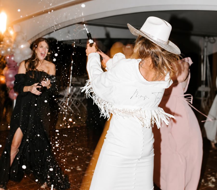 Friends spraying champagne, the bride to be in a wide-brimmed hat