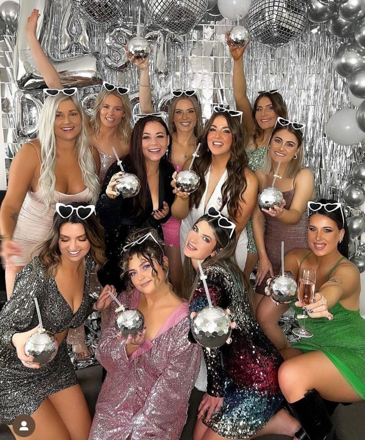 A hens group in sequins holding disco ball cups in front of a silver wall