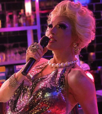 A blonde drag performer in sequins singing into a microphone