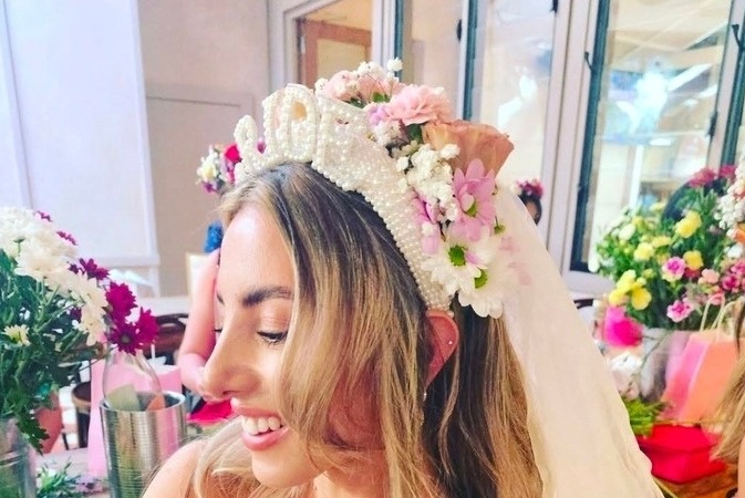 The bride in her veil and a crown of pearls and flowers, smiling beside buckets of fresh blooms