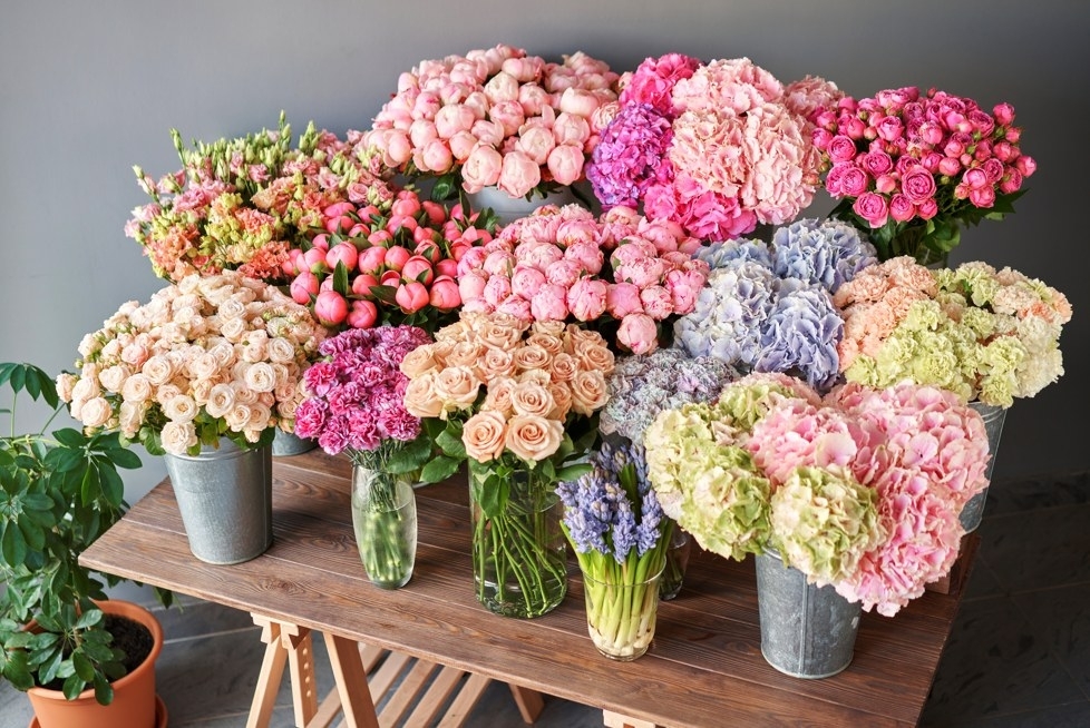 Buckets of fresh pink, white and purple flowers lined up on a wooden table, ready for crown making