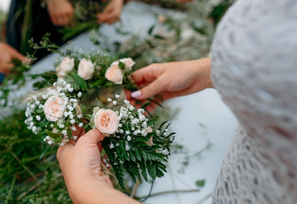 Hands working soft white blooms and greenery into a flower crown