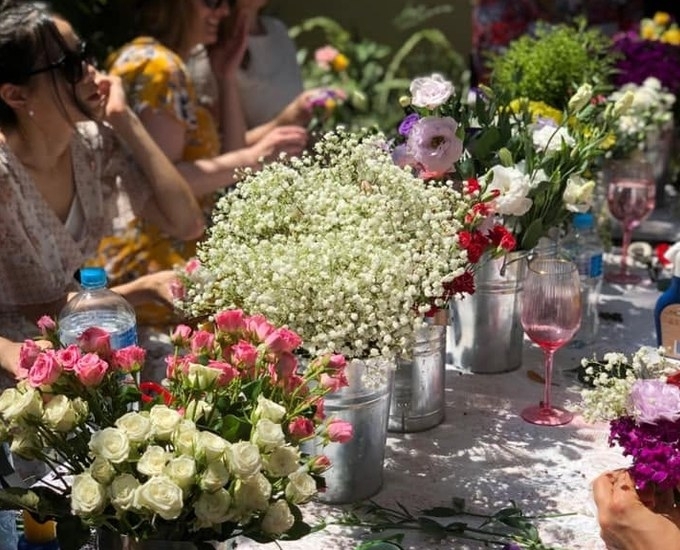 Buckets of flowers on a lace table as friends make their crowns in the sun