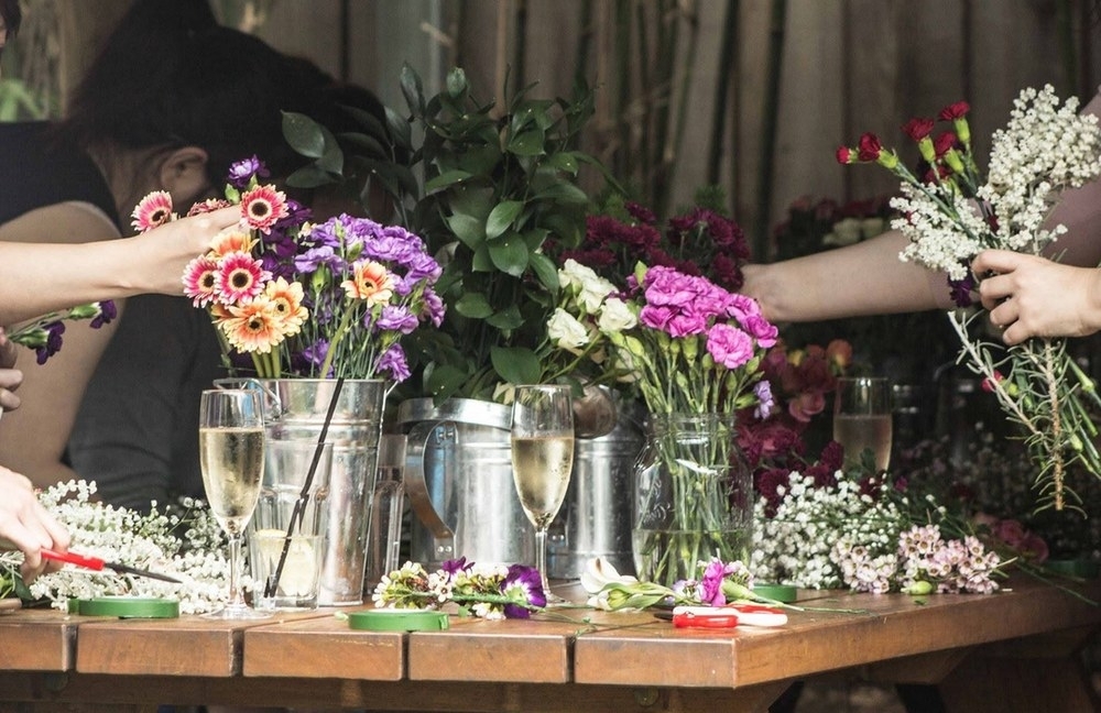A workshop table of fresh pink and white flowers with glasses of bubbly ready for crown making