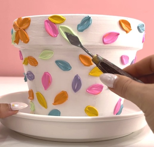 A hand painting coloured petals onto a white terracotta pot