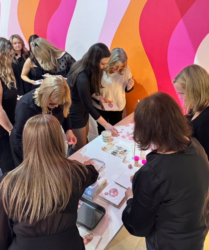 A crew in black gathered round a table of pink clay pieces in front of a pink and orange wavy wall