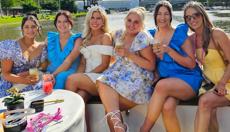 The bride in her tiara with her crew on deck, drinks in hand, the river and the city behind them