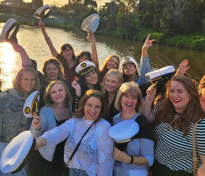 A big hens crew of every age throwing captain hats in the air on a river cruise at sunset