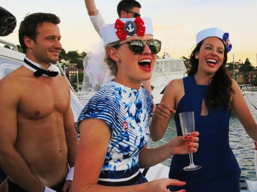Our topless waiter in his bow tie on a yacht with the bride in her sailor hat and veil and a friend, both mid laugh