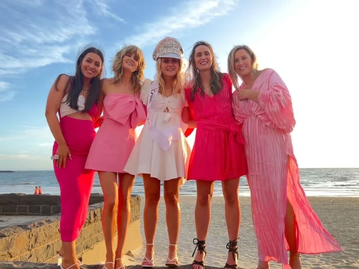 Five friends in pink dresses on a beach at golden hour
