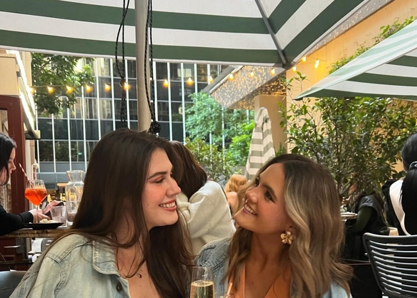Two friends with glasses of bubbly at a sunny waterfront table