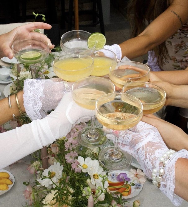 Hands in white lace gloves raising coupes over a table of fresh flowers