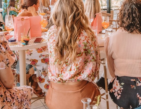 A hens crew in florals seated along tables with spritzes and pink gift bags