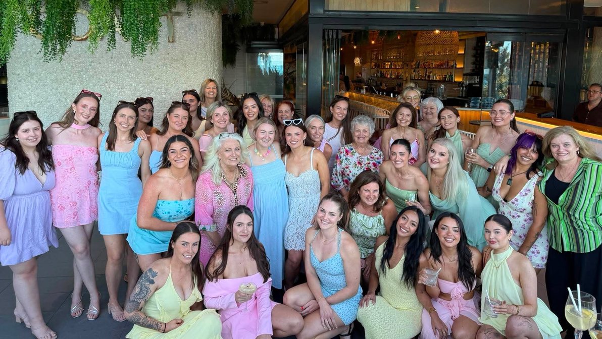 A large hens group of all ages in pastel dresses together at a venue