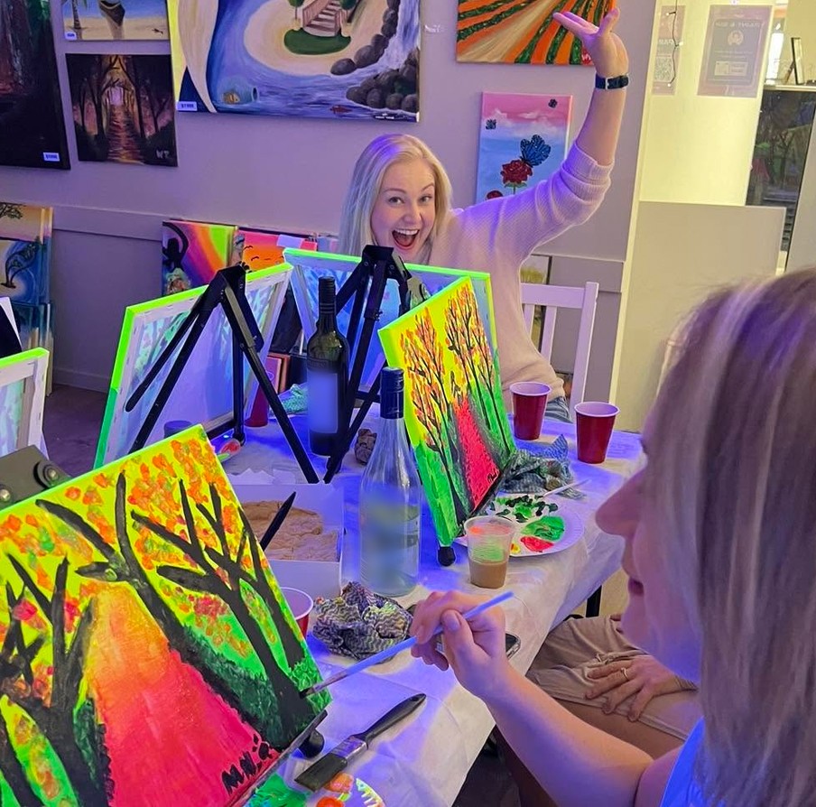 A guest throwing her arm up in delight across a table of glowing tree paintings