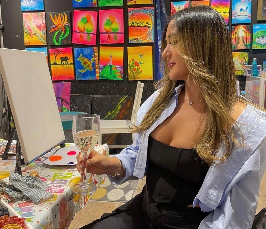 A guest with a glass of bubbles eyeing her blank canvas in a studio hung with bright paintings