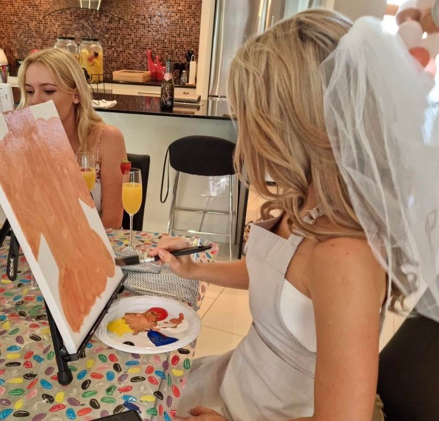 The bride in her veil painting at an easel, a glass of bubbles beside her