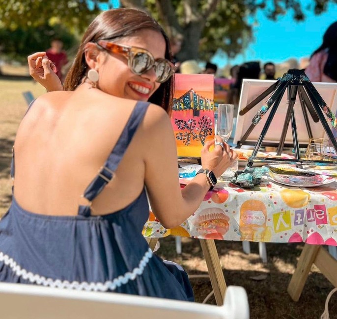 A guest in sunglasses and a backless navy dress laughing over her shoulder at an outdoor painting table