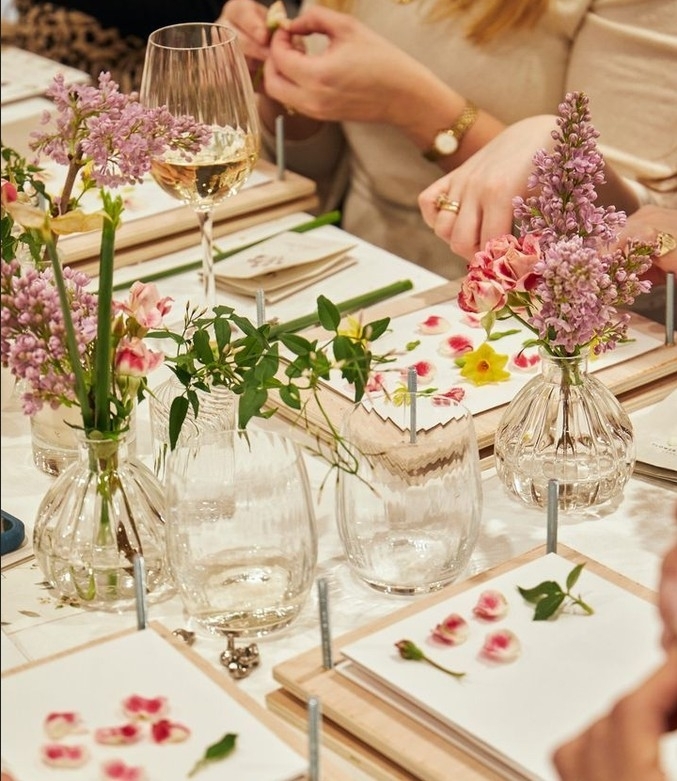 A perfume table of flowers in glass vases with fresh petals laid out on cards