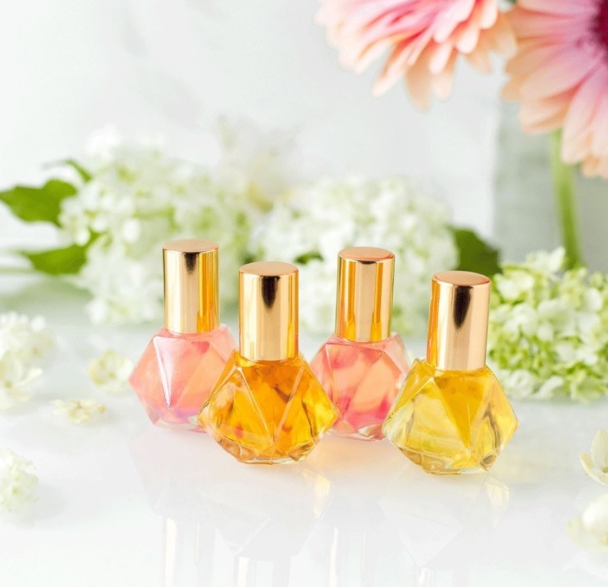 Four gem-shaped perfume bottles in pink and amber among white flowers