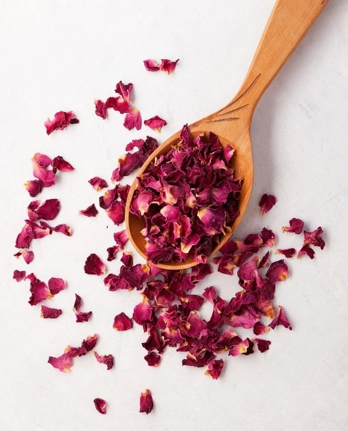 A wooden spoon heaped with dried rose petals
