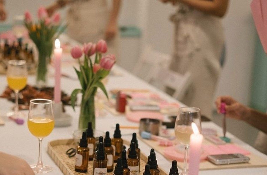 A long perfume table set with pink tulips, candles, amber bottles and a drink at every seat