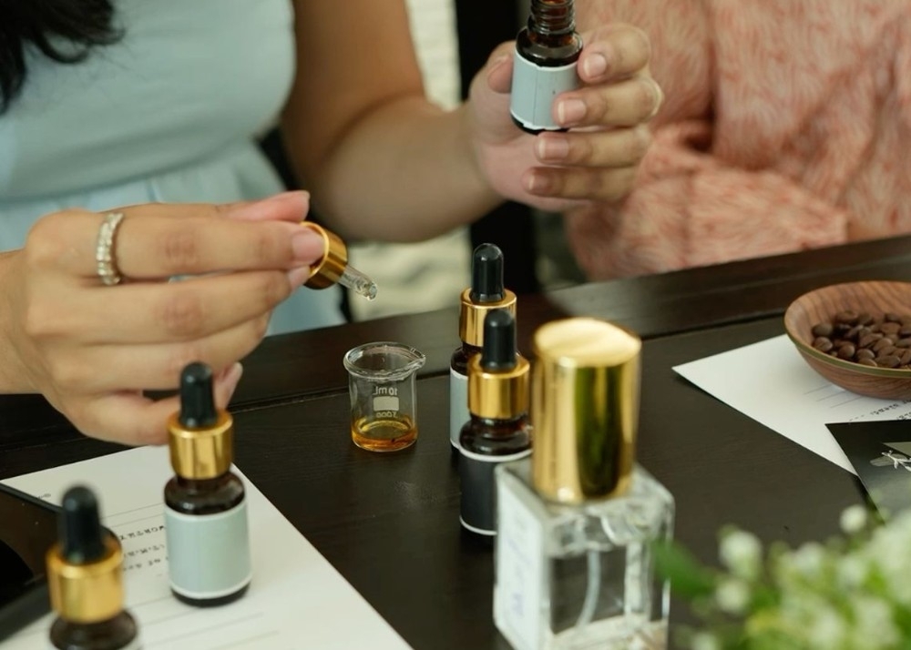 Two friends blending with dropper bottles, a gold-capped perfume bottle in front