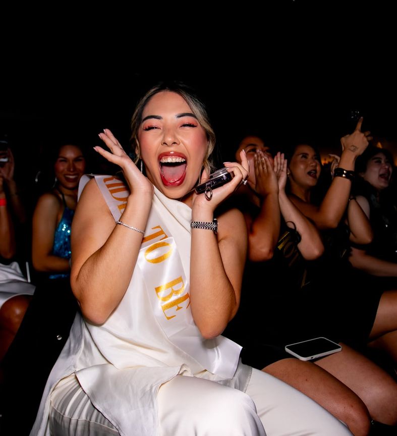 The bride to be in her sash screaming with joy, her friends behind her screaming just as loud