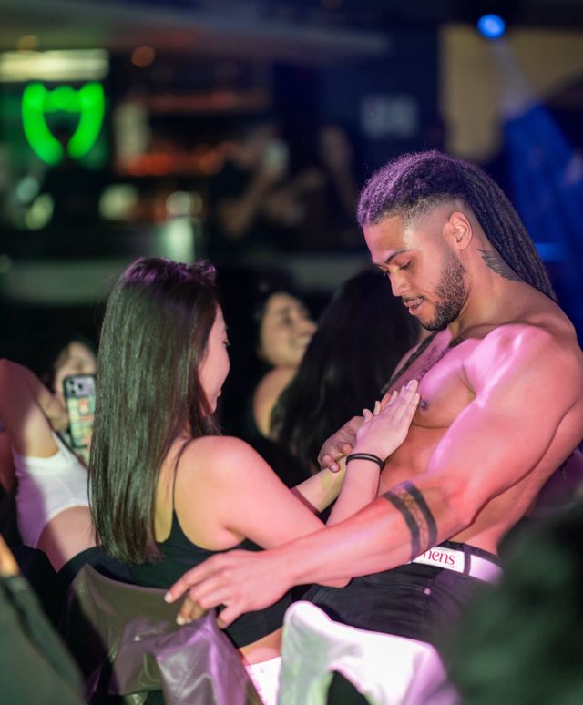 A hen with her hand on a shirtless performer's chest while her friends film on their phones