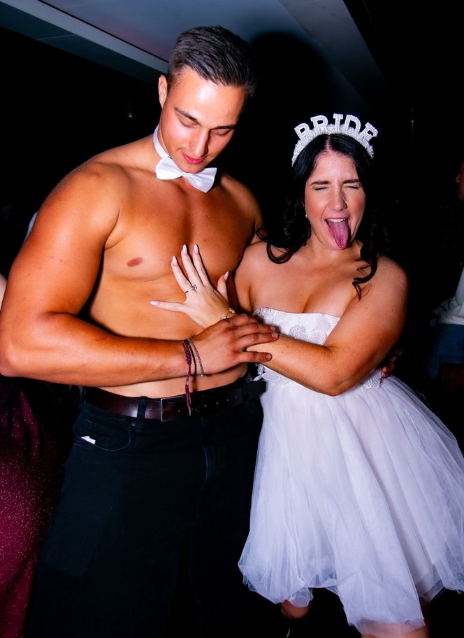 The bride in her BRIDE tiara poking her tongue out, her hand on our topless waiter's chest