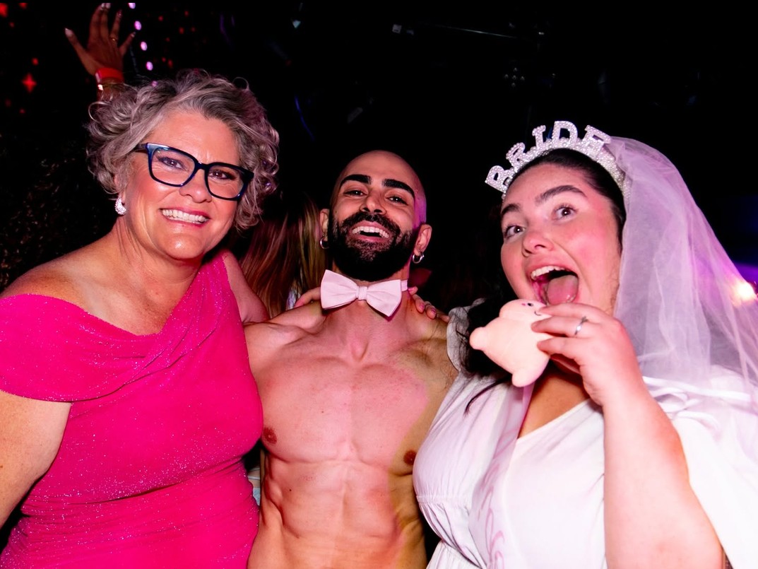 The bride in her Bride tiara and veil hamming it up with our topless waiter and a guest in hot pink