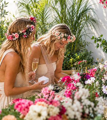 Two friends in flower crowns arranging flowers at a table