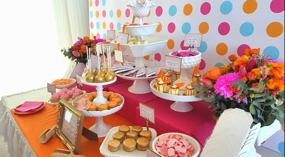 A hens dessert table with cake stands, little cakes and a big bunch of orange and pink flowers