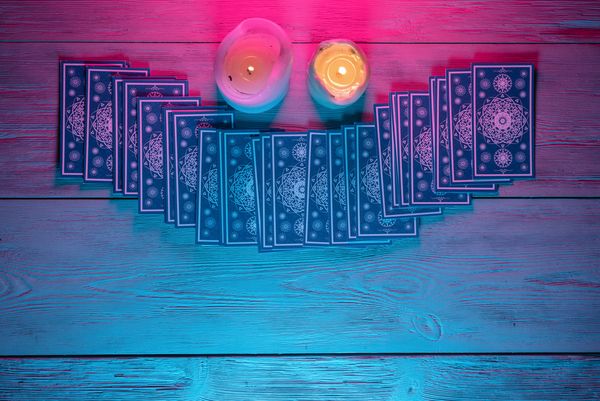Tarot cards fanned across a pink and blue table between two candles