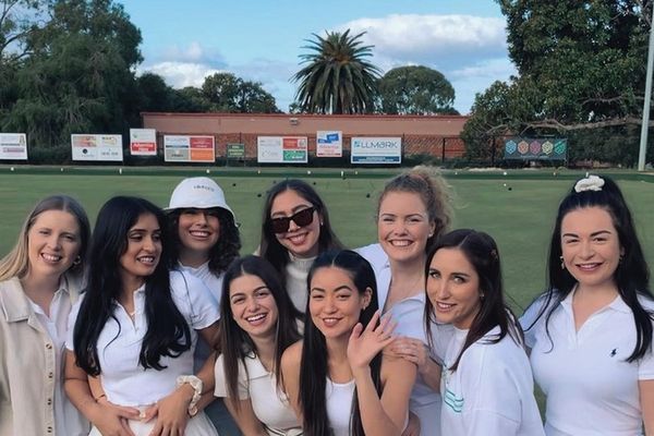 Group of women in white outfits smiling together beside a sunny lawn bowls green