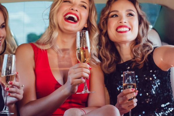 Two friends laughing with glasses of bubbly in the back of a limousine